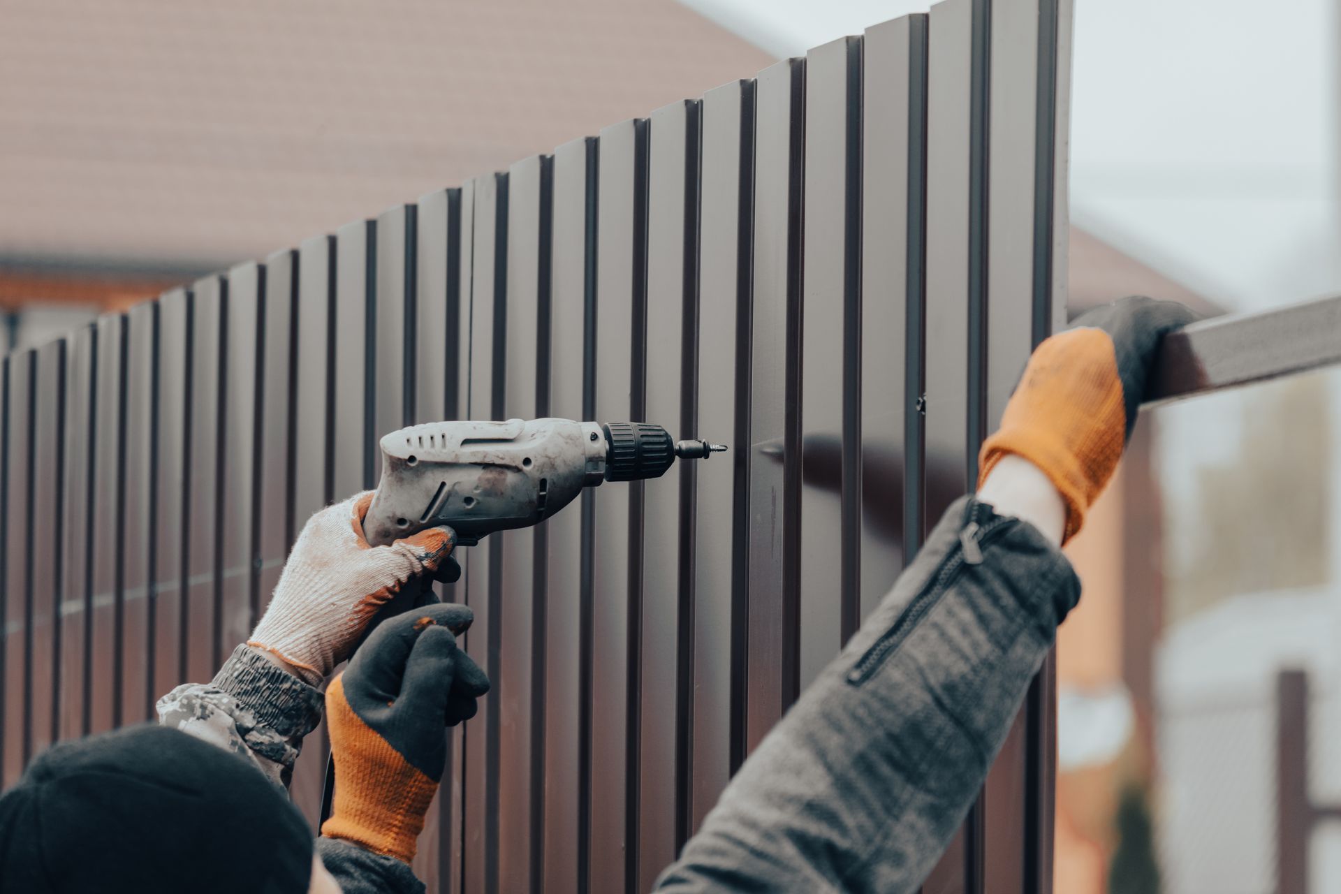 Workers installing a dark vertical slat fence with a drill outdoors